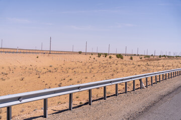 A long, empty road with a fence on the side. The fence is made of metal and is very tall. The road is surrounded by a desert landscape