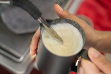 a person holding a pitcher, steaming milk for pouring latte art