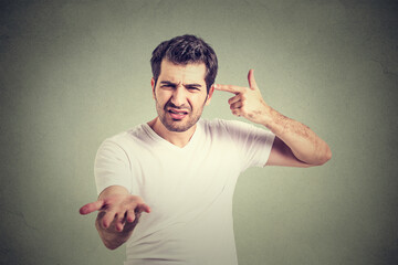 angry young man gesturing with his finger against temple are you crazy? Isolated on gray wall background. Negative emotion facial expression 