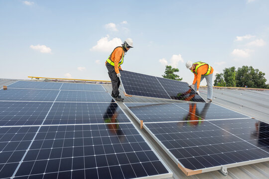 Men technicians carrying photovoltaic solar moduls on roof of factory on the morning. Installing a Solar Cell on a Roof. Solar panels on roof. Workers installing solar cell power plant eco technology.