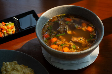 Sop iga (beef rib soup), an indonesian dish served with rice and emping or melinjo chips, on wooden table surface, cafe environment