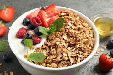 Tasty granola with berries and yogurt in bowl on grey textured table, closeup