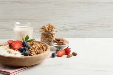 Tasty granola with berries and yogurt in bowl on white marble table, closeup. Space for text