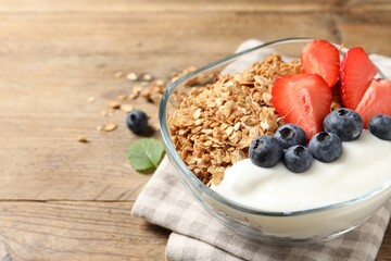 Tasty granola with berries and yogurt in bowl on wooden table, closeup. Space for text
