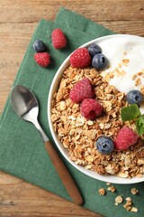Tasty granola with berries and yogurt served on wooden table, top view