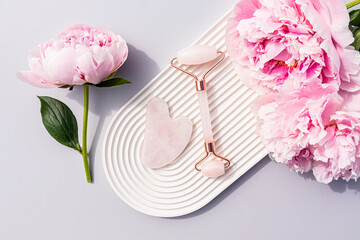 Rose quartz roller massager and gua sha scraper on a white ceramic tray with a delicate pink...