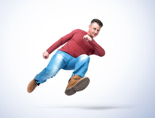 Full length handsome man in casual clothes runs quickly jumping high, isolated on a light blue...