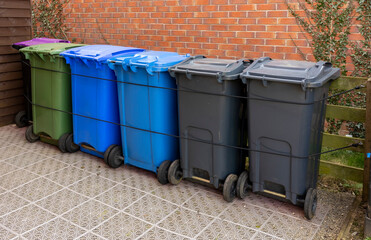 UK recycling wheelie bins of different colours lined up in garden storage area