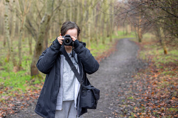 Young photographer teenage girl using DSLR camera outdoors in wood taking photos