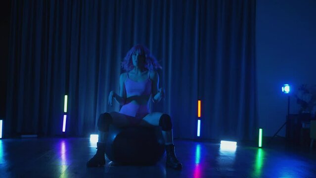 Young woman in pink wig in anime style, in dimly-lit neon room, erotically dancing twerk. Half-shaven Girl moving seductively gracefully in darkened space. Striptease in a disco club on stage. Cheers 