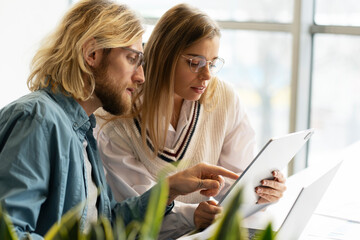 Portrait of confident colleagues working together using laptop and digital tablet