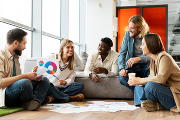 Diverse team of young professionals having working meeting sitting on floor