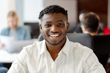 Obraz premium Young black man smiling in busy open plan office