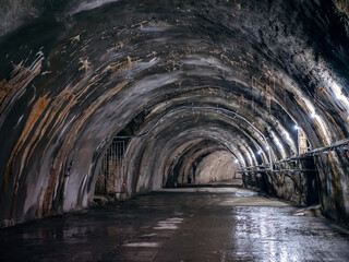 Naklejka premium Old industrial arched tunnel with concrete walls, dim artificial lighting, and dripping water.