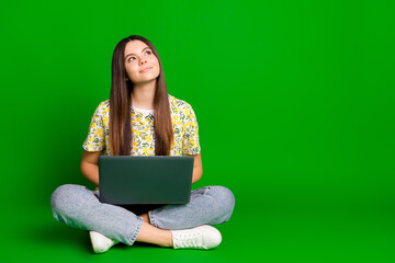 Full length photo of lovely teen lady sit floor netbook look empty space dressed flowers print garment isolated on green color background