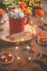 Cute cozy winter composition. red mug, marshmallows, oranges and Christmas lights.