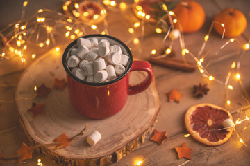 Cute cozy winter composition. red mug, marshmallows, oranges and Christmas lights.