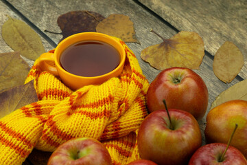 Autumn still life on a wooden background. A cup of tea, a scarf, apples and dry autumn leaves create an autumn atmosphere. Bright autumn.