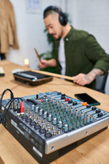 Close-up of a sound mixer in a studio with a blurry image of an Asian man playing an instrument in the background.