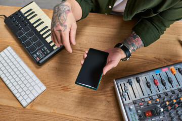 A handsome Asian man, a multi-instrumentalist, working in his studio, pauses to check his phone.