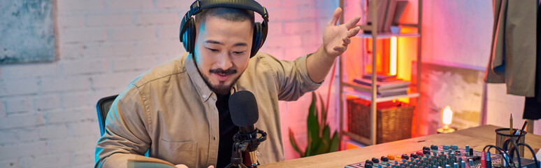 A man with headphones records a podcast in his studio, looking directly at the microphone.