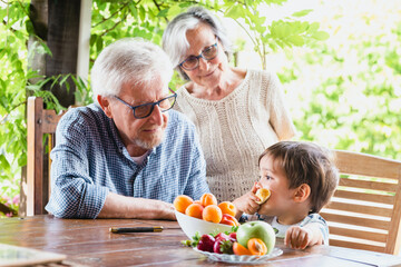 A young boy eating fruit with his grandparents at a table outdoors. Healthy family living habits.