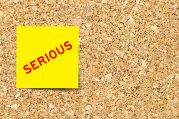 Yellow note paper with word serious on cork board background with copy space