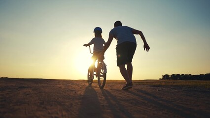 family play in the park. father teaching daughter to ride a bike. happy family kid dream concept. daughter learn to ride a bike silhouette. father supporting child riding sunset bike summer in park