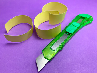 Green paper knife on purple background with pieces of yellow paper.