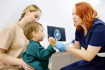 Baby and his mother are being seen by a pediatric neurologist in medical clinic. Doctor conducts tests, checks the reflexes, hearing of small patient using tuning fork. Highly qualified cure