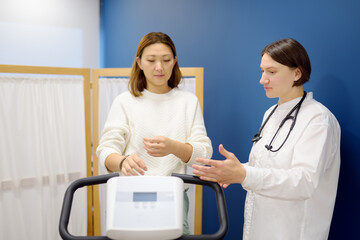 A female cardiologist tests a patient during a bike workout to check the cardiovascular system in the clinic's medical office. A young woman trains on an exercise bike.