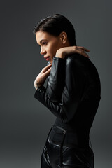 A woman in black leather jumpsuit poses with a seductive gaze.