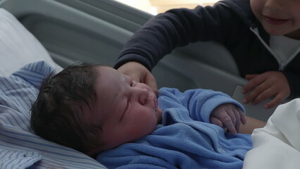Sibling intercts with newborn baby brother at hospital resting in bed after birth, initial days of...