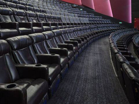 This image captures an empty IMAX cinema hall with multiple rows of black leather seats. The seats are arranged in a tiered fashion, ensuring an unobstructed view of the screen for every viewer. 