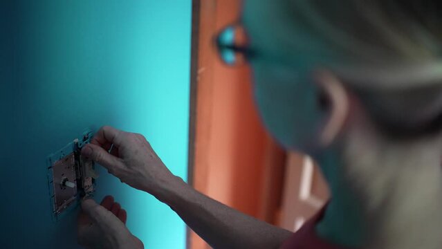 Over shoulder view of mature woman using installing electrical light switch in a home remodeling improvement project.