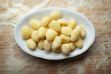 Potato gnocchi with durum wheat flour in ceramic dish on pastry board, top view, close-up.
