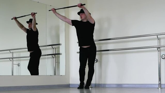 Jazz dance or caberet rehearsal in the studio with a cane, a young guy in a gangster hat. Creative dance blues man, in black clothes with a stick in his hands