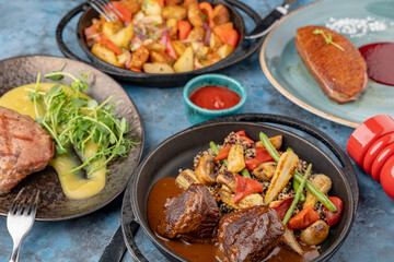 A table served with dishes of meat, vegetables, potatoes and herbs.