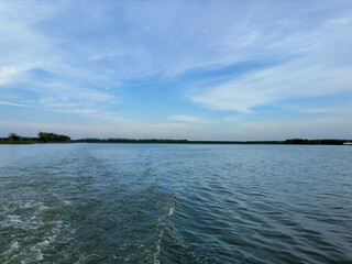 A vast expanse of a serene water body covered with lush green lily pads, extending towards the horizon under a calm and cloudy sky. The tranquil scene is accentuated by the reflection of the sky and c