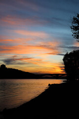 Fototapeta premium sunset in the city near the river. silhouettes of houses and bridge in the background