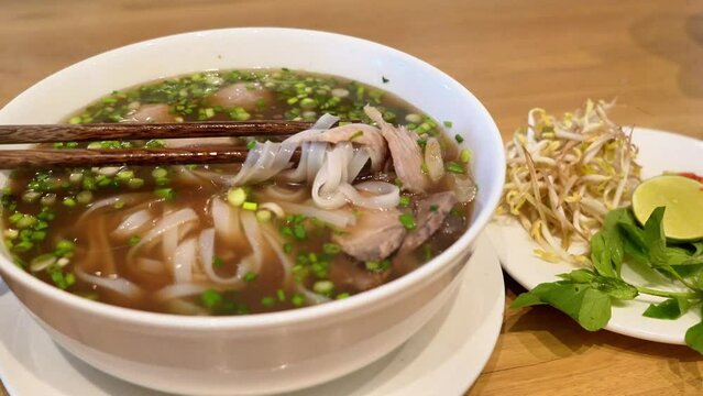 a bowl of Vietnamese pho with thin rice noodles, sliced beef, fresh herbs, and lime wedge. Pho is a fragrant noodle soup perfect for any meal.