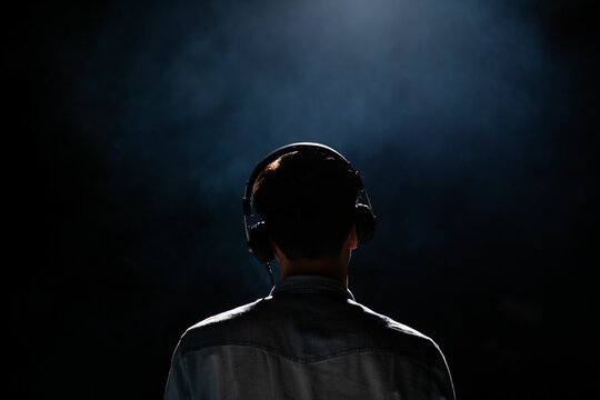 Back view of a man wearing headphones in a dark room with a spotlight illuminating him