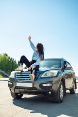 A girl sits on the hood of a car on a sunny summer day.