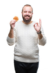 Young caucasian hipster man eating sweet waffle over isolated background doing ok sign with fingers, excellent symbol