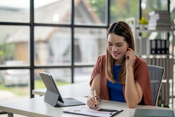 Fototapeta premium A woman is sitting at a desk with a laptop and a tablet