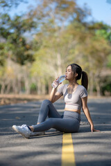 A woman is sitting on the road drinking water