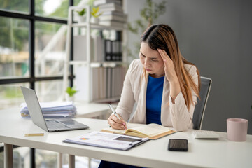 Obraz premium A woman is sitting at a desk with a laptop and a notebook