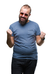 Fototapeta premium Young caucasian hipster man wearing sunglasses over isolated background very happy and excited doing winner gesture with arms raised, smiling and screaming for success. Celebration concept.