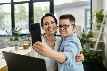 Obraz premium A mother working in her office takes a selfie with her son, who has Down syndrome, demonstrating a positive and inclusive work environment.