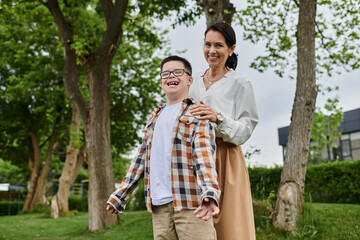 A mother and her son with Down syndrome are walking together outdoors, showcasing a heartwarming moment of family togetherness.